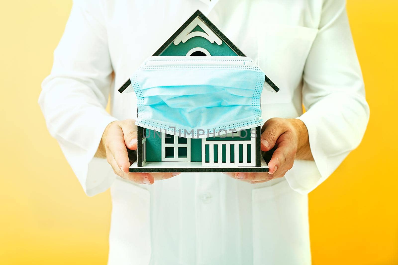 Model house in the hands of a doctor, house with protective medical mask. Safety to stay at home