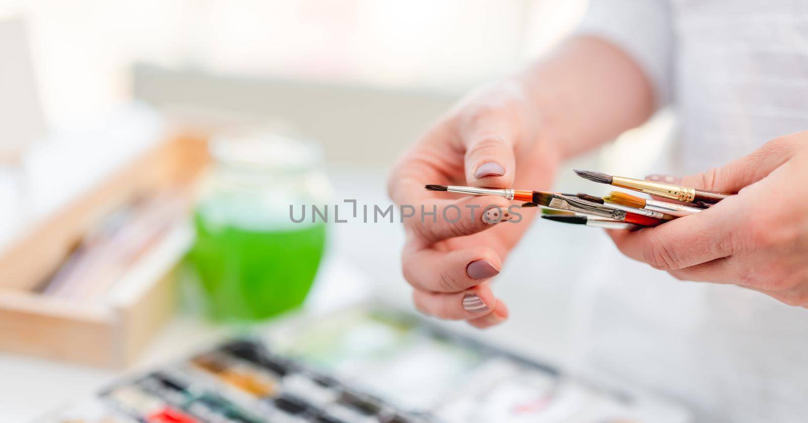 Artist woman holding different painbrushes in her hands and choosing one during drawing process