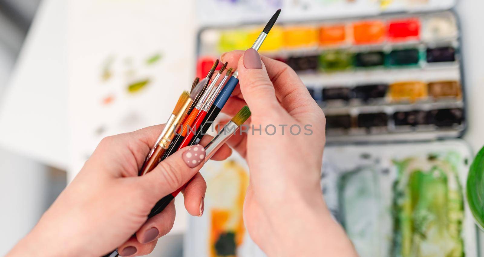 Woman artist hands holding paintbrushes and choosing one for drawing with watercolor