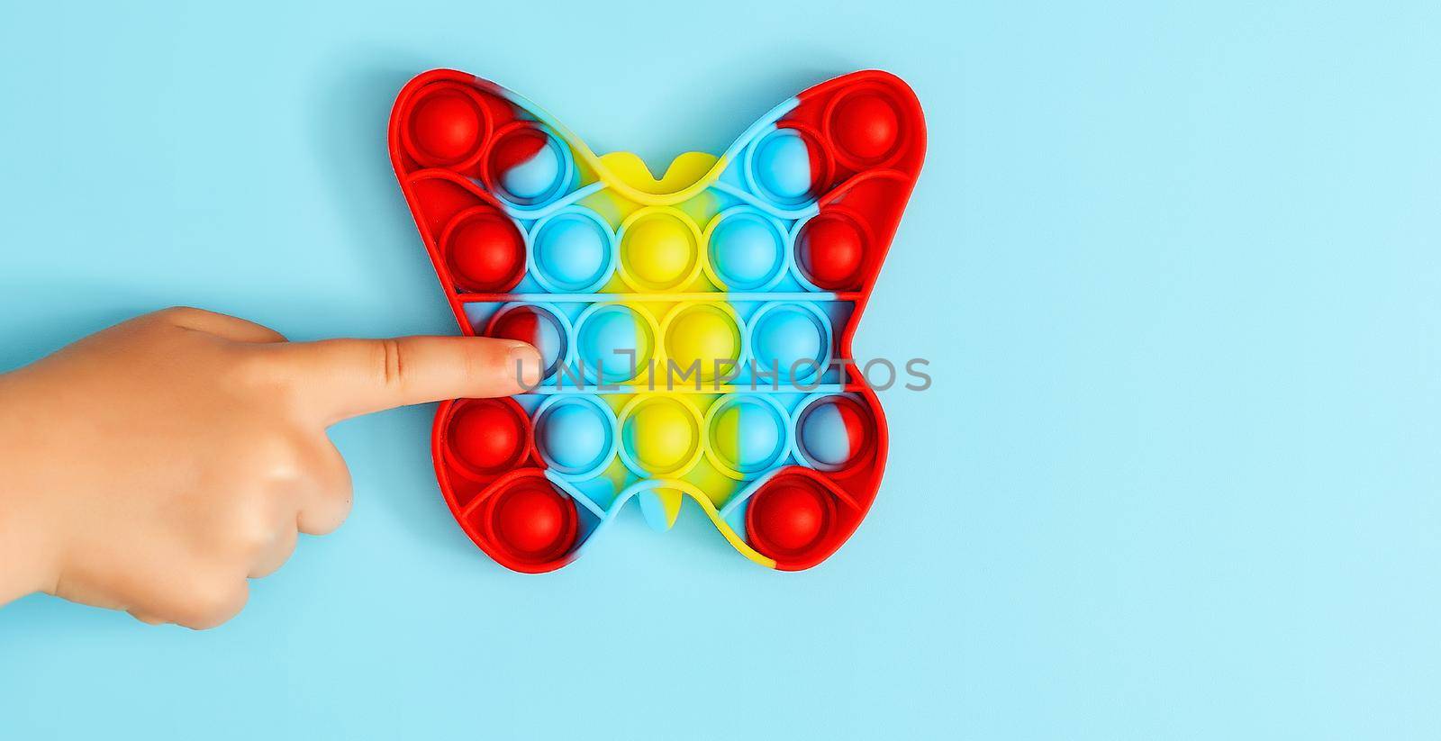 Trendy toy antistress. Anonymous child with colorful poppit game. Image of trendy Pop it fidget toy . Top view of the new sensory toy