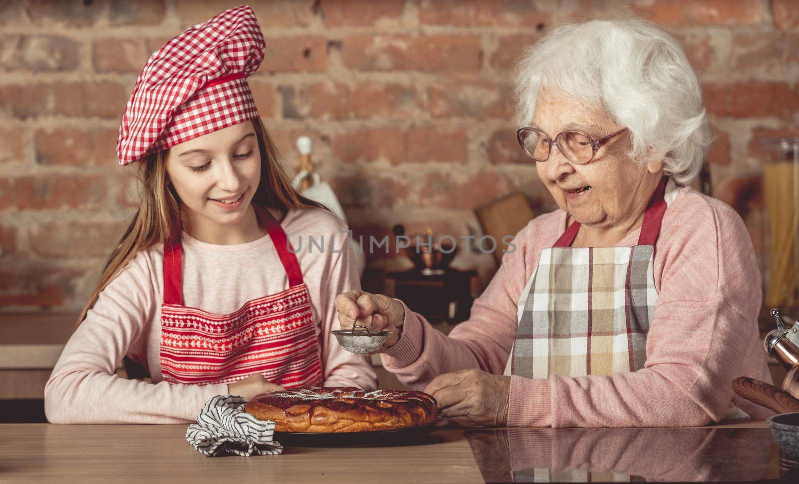Granny with her little chef girl sprinkle with powder hot homemade pie