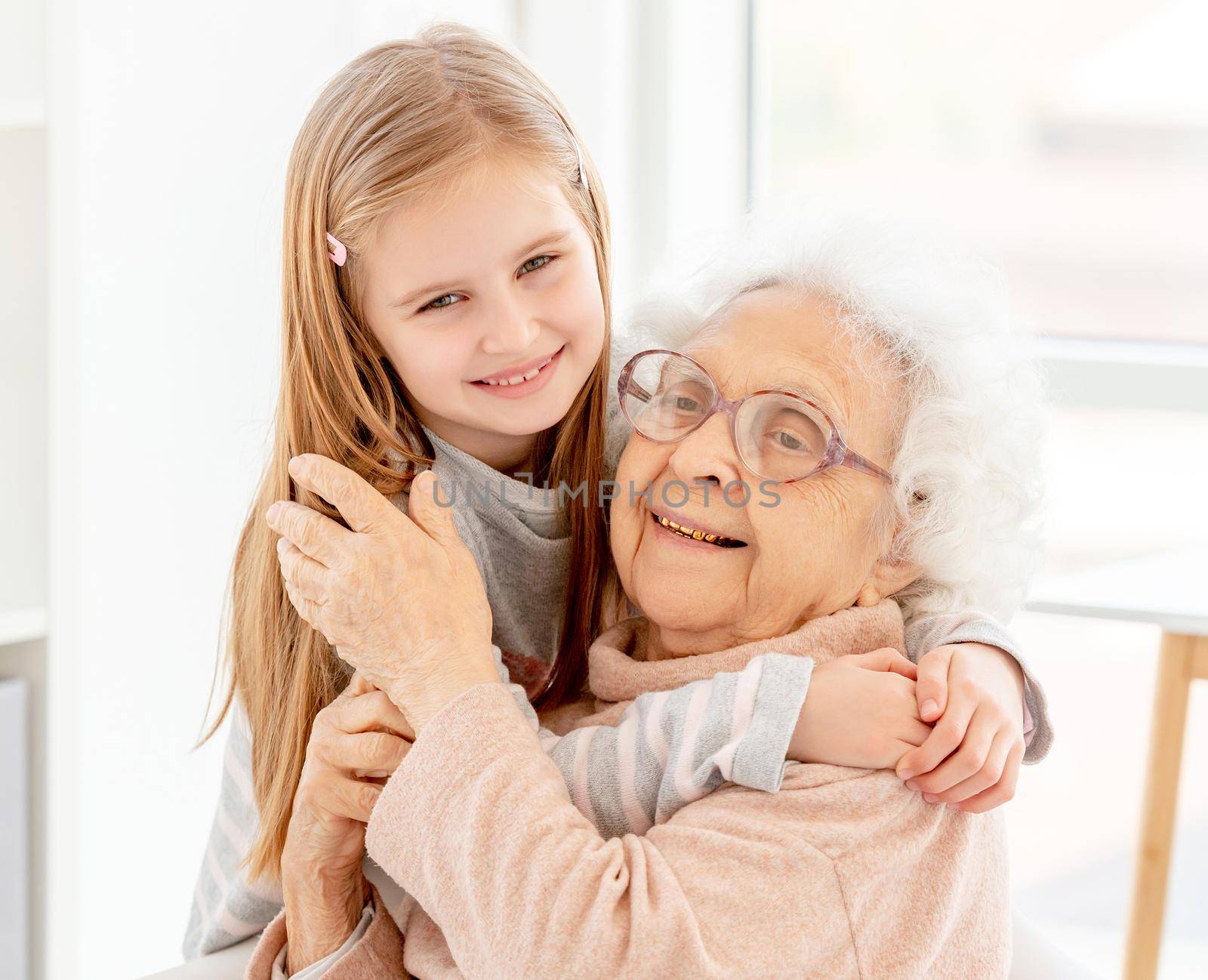 Happy little girl embracing grandmother indoors