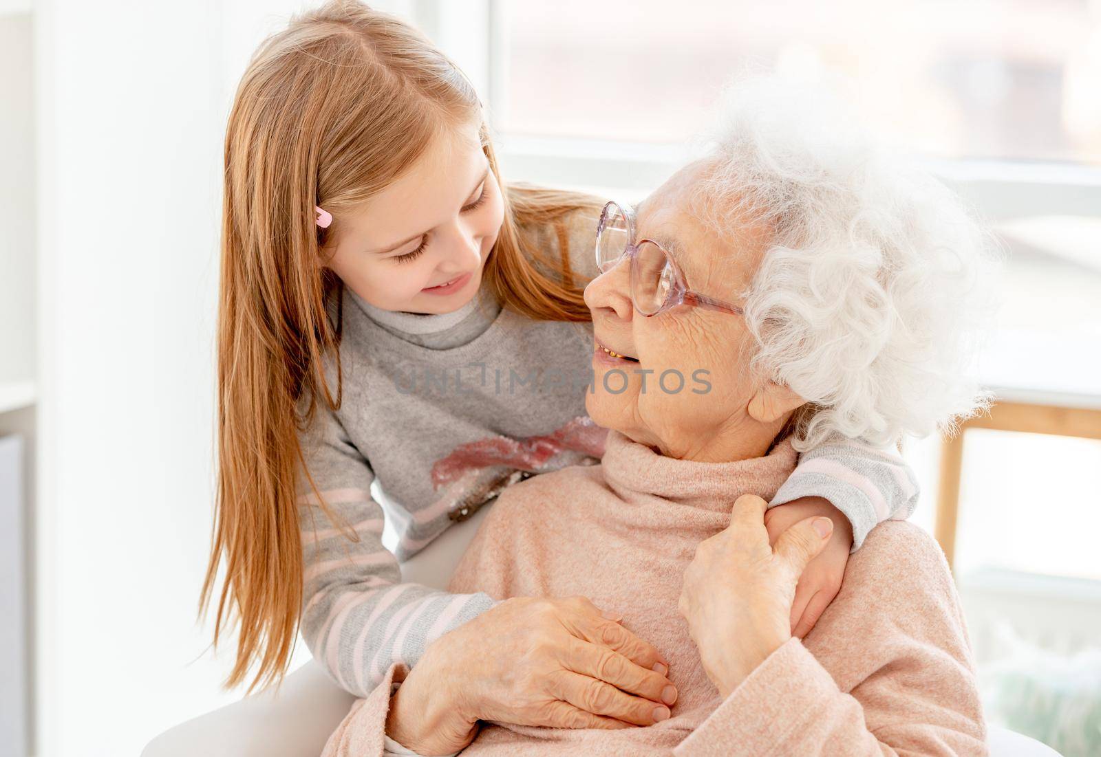 Lovely aged woman and little girl looking at each other at home
