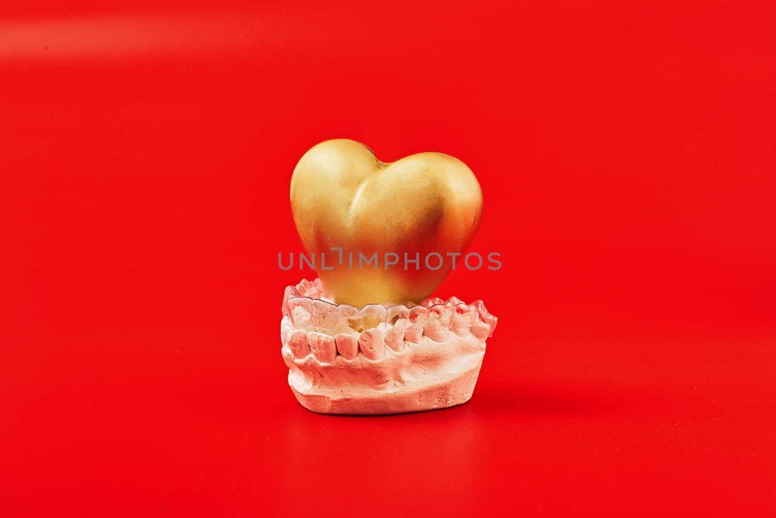 Heart of gold on a red background in invisible dental aligners or braces aplicable for an orthodontic dental treatment by Maximusnd
