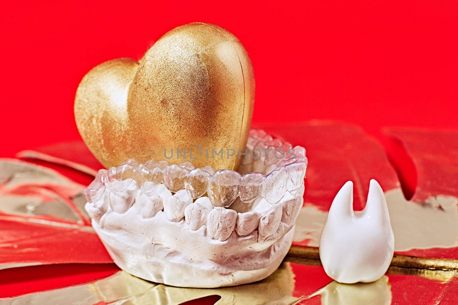 Heart of gold on a red background in invisible dental aligners or braces aplicable for an orthodontic dental treatment by Maximusnd