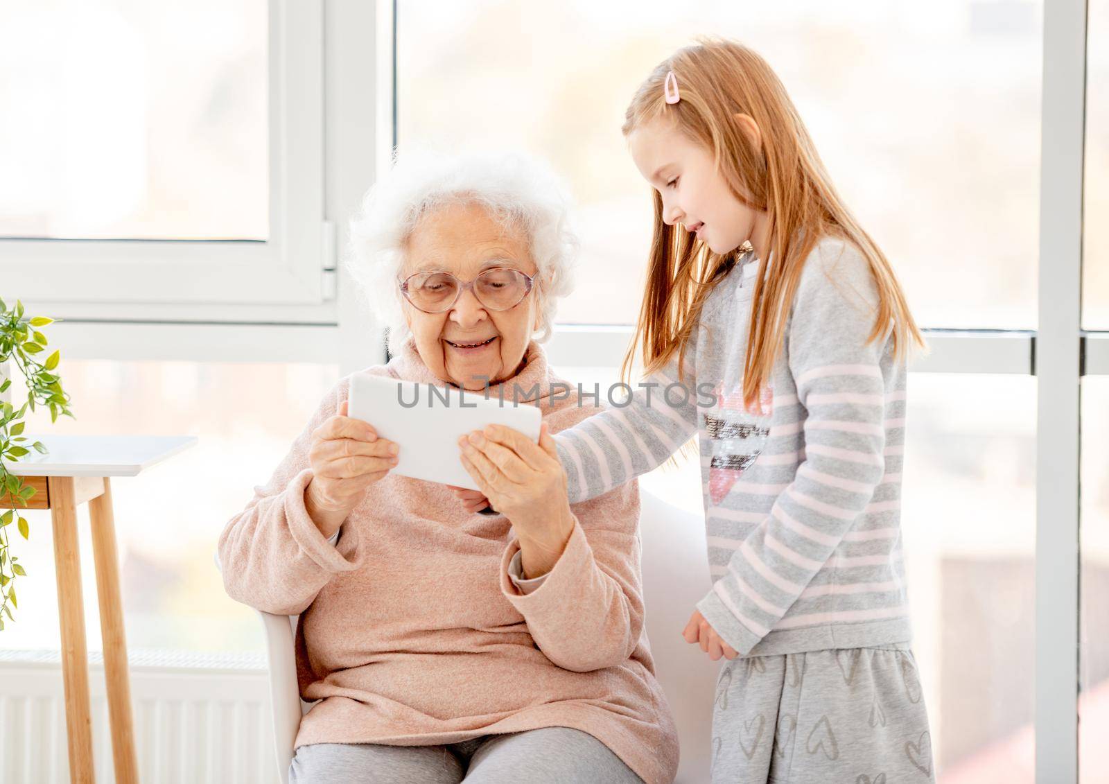 Cute little girl teaching great-grandmother to use new technologies