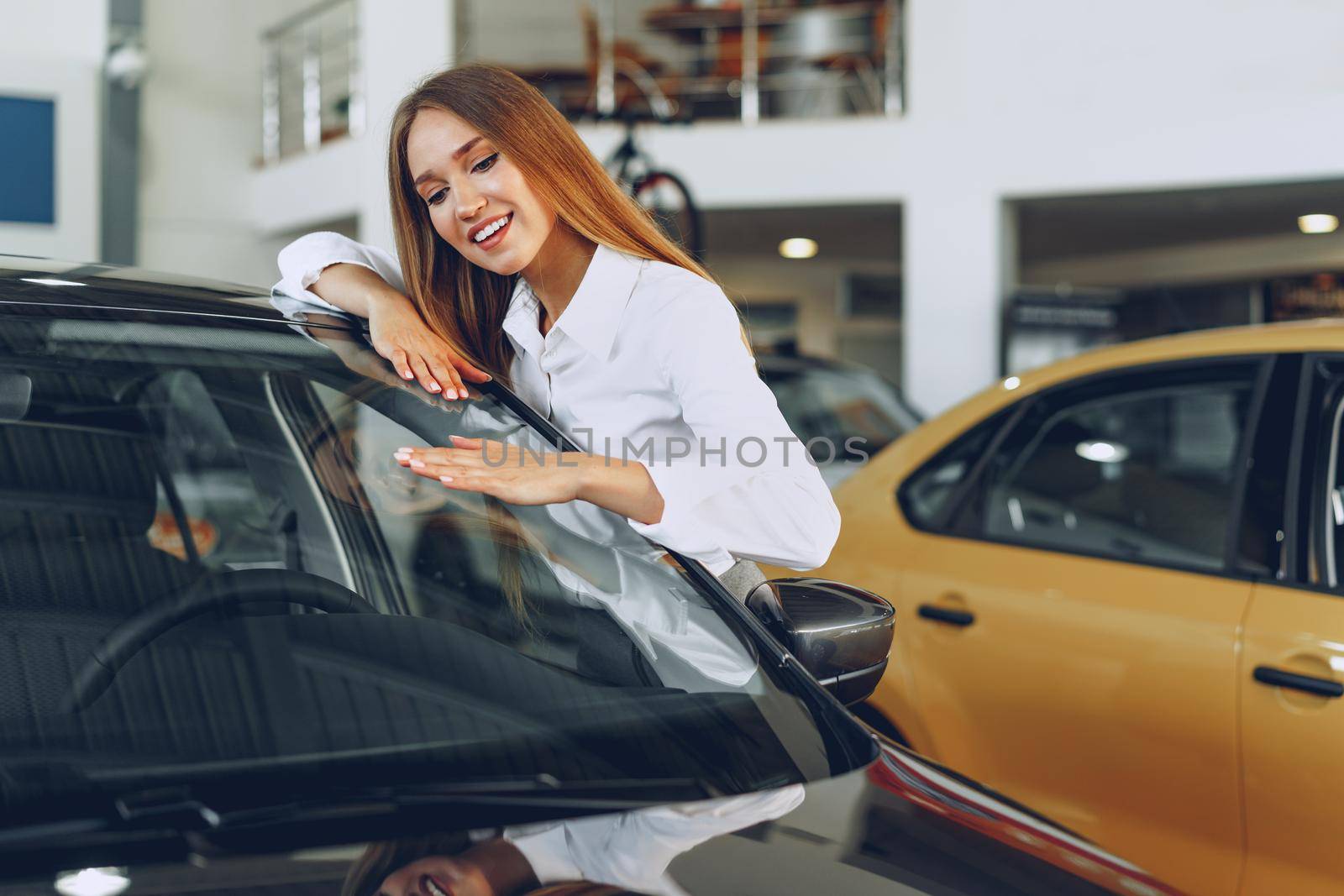 Beautiful young woman touching her new car with pleasure and joy