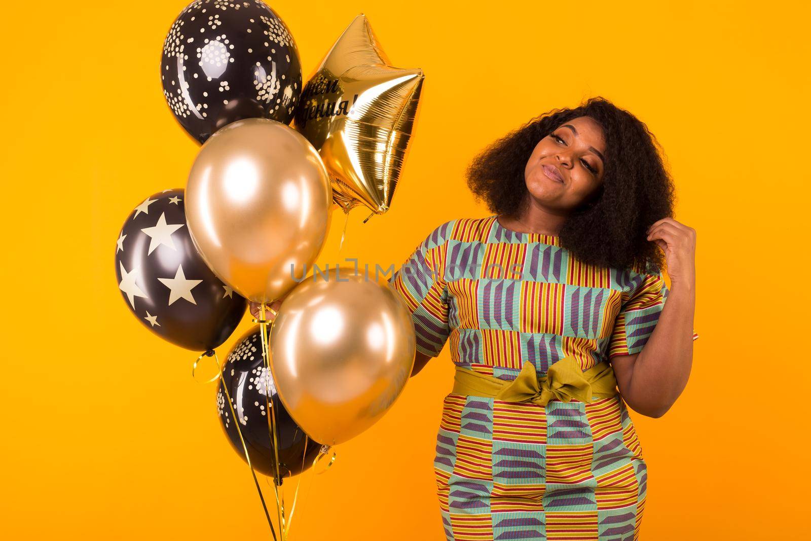 Holidays, birthday party and fun concept - Portrait of smiling young African-American young woman looking sweet on yellow background holding balloons. by Satura86