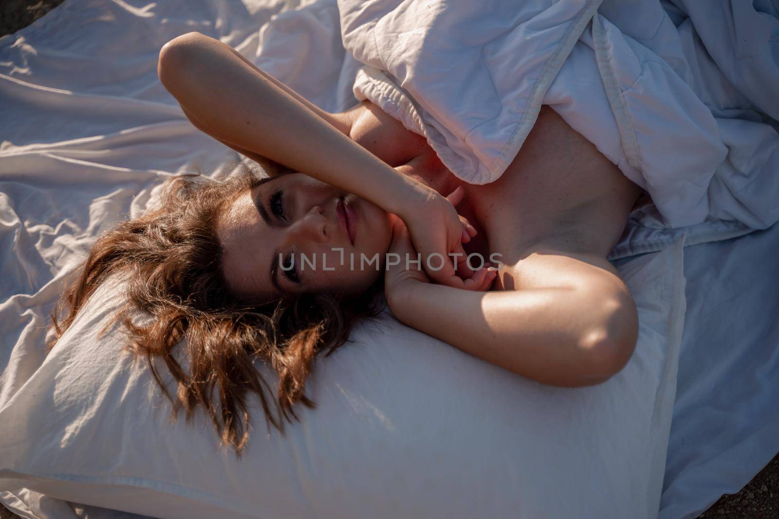 Woman wearing pajamas wake up in bed wuth duvet and pillow over nature sea background outdoors. Back view. Good morning. Freedom concept. by Matiunina