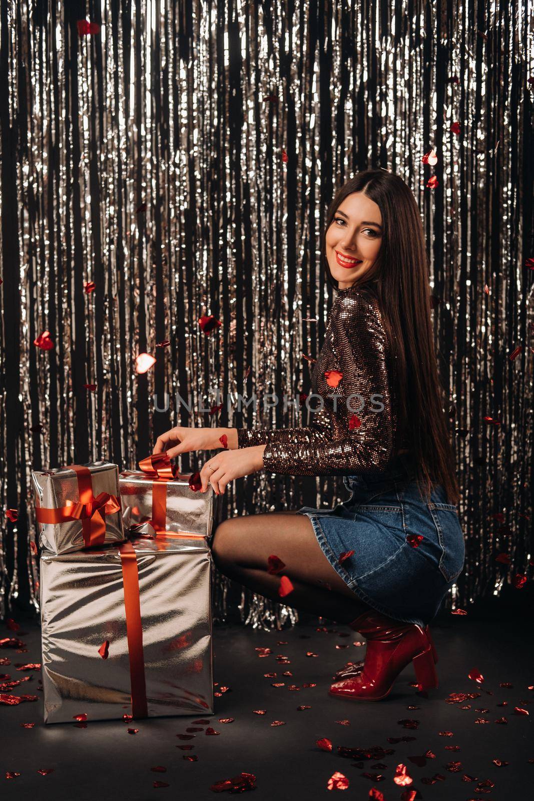 a girl in a shiny jacket and skirt with gifts on a silver background in the form of rain.