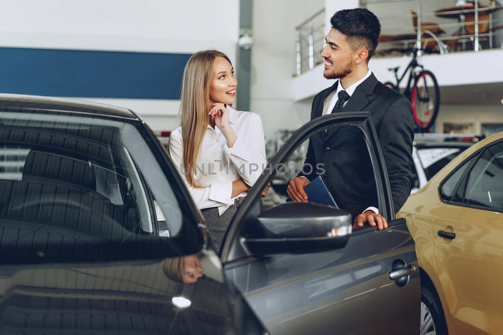 Man car dealer showing a woman buyer a new car in car salon