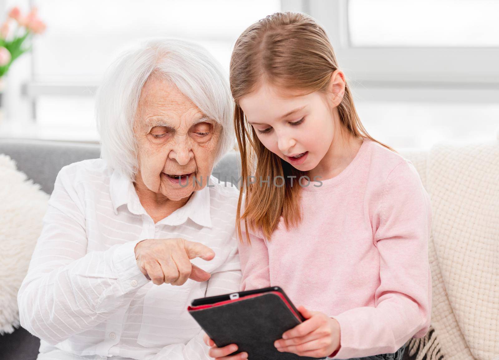 Grandaughter teaching grandmother use tablet. Family portrait at home with gadgets