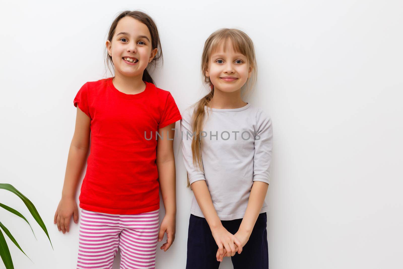 Cute little caucasian girls are keeping hands up, looking at camera and smiling, isolated on a white background by Andelov13
