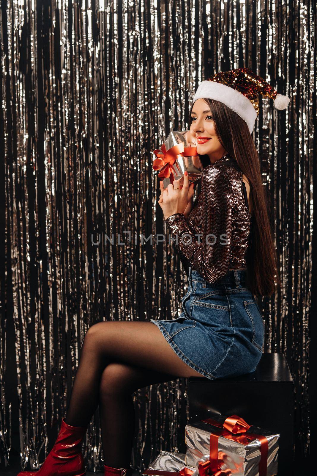 a girl in a shiny jacket with a Santa hat with gifts on a silver background in the form of rain.