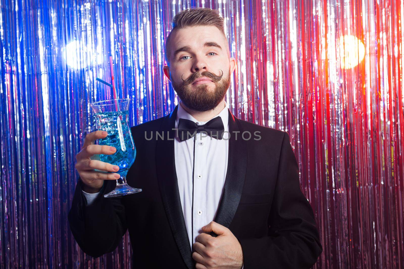 Portrait of elegant handsome man in a expensive suit holds blue cocktail on shiny background