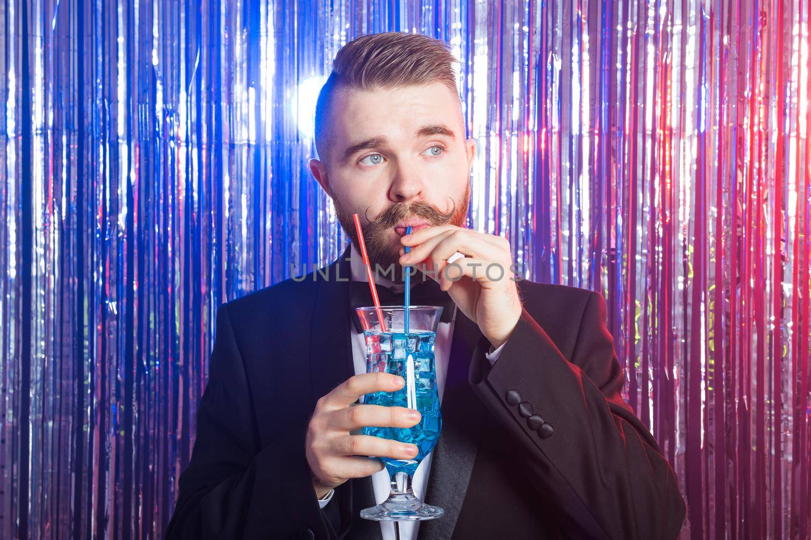 Portrait of elegant handsome man in a expensive suit holds blue cocktail on shiny background