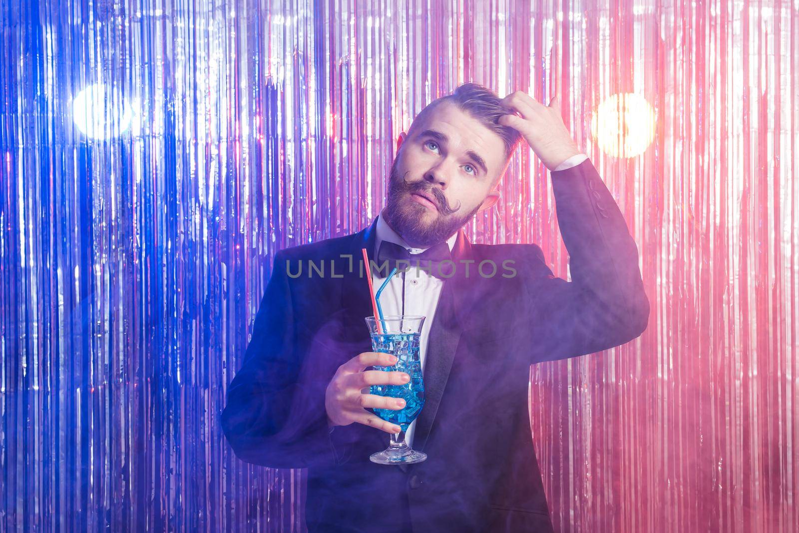 Portrait of elegant handsome man in a expensive suit holds blue cocktail on shiny background