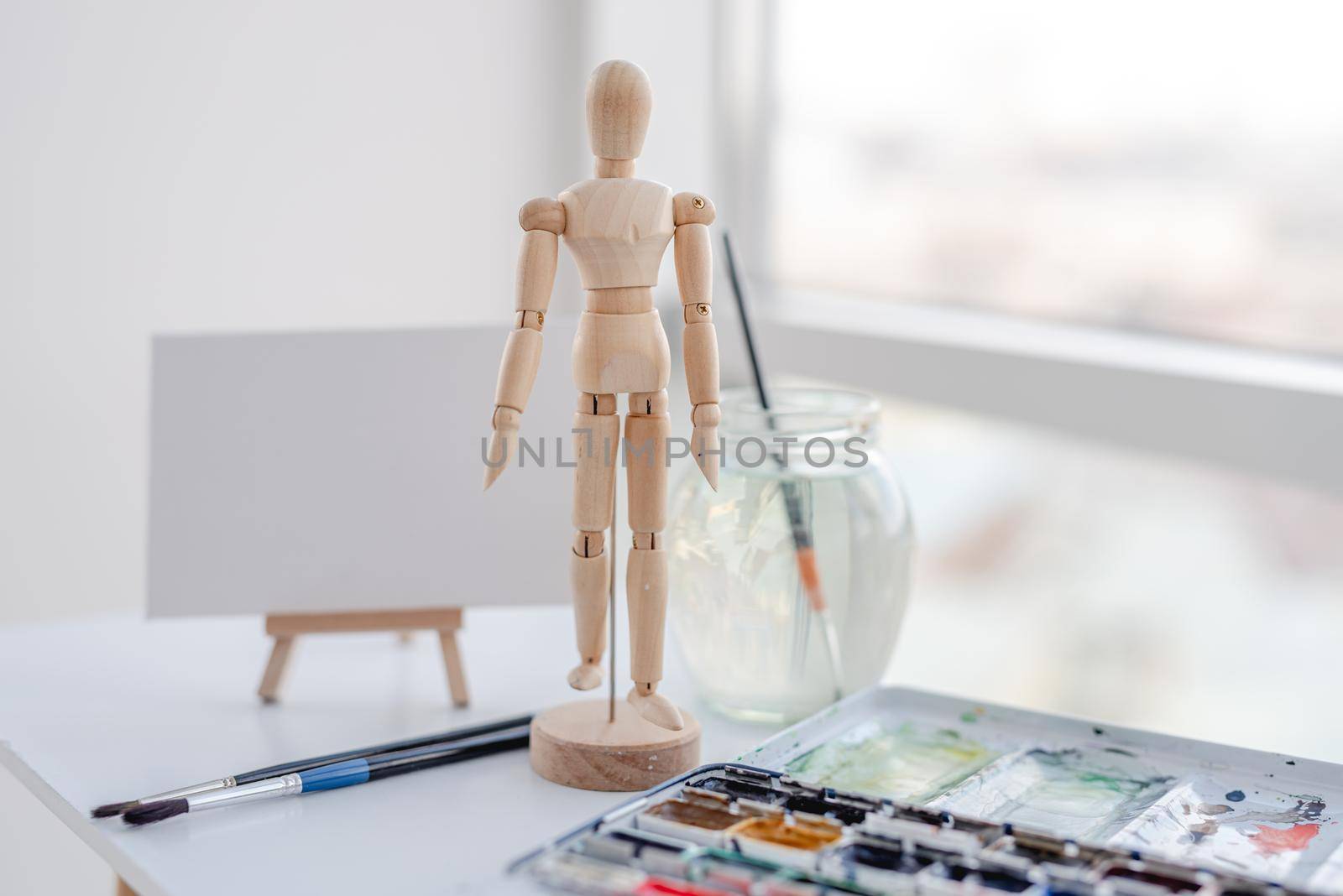 Dummy wooden man for painting and watercolor on the table with easel on background