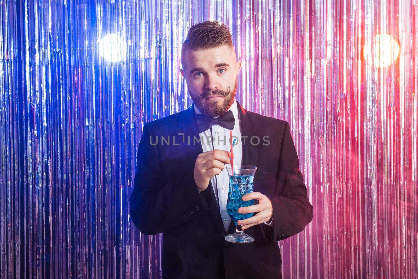 Portrait of elegant handsome man in a expensive suit holds blue cocktail on shiny background