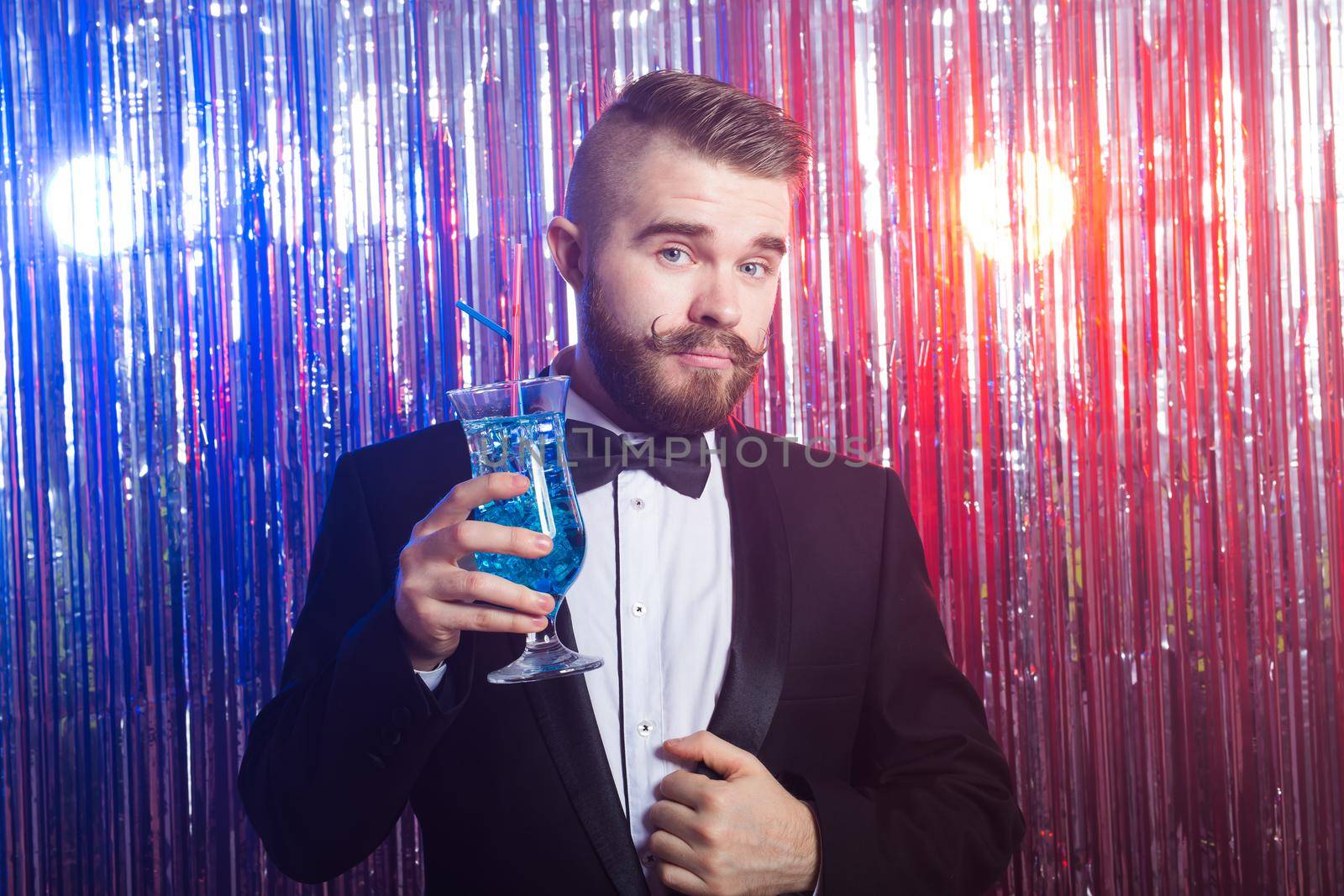 Club party and holidays concept - Portrait of elegant handsome man in a expensive suit holds blue cocktail on shiny background. by Satura86