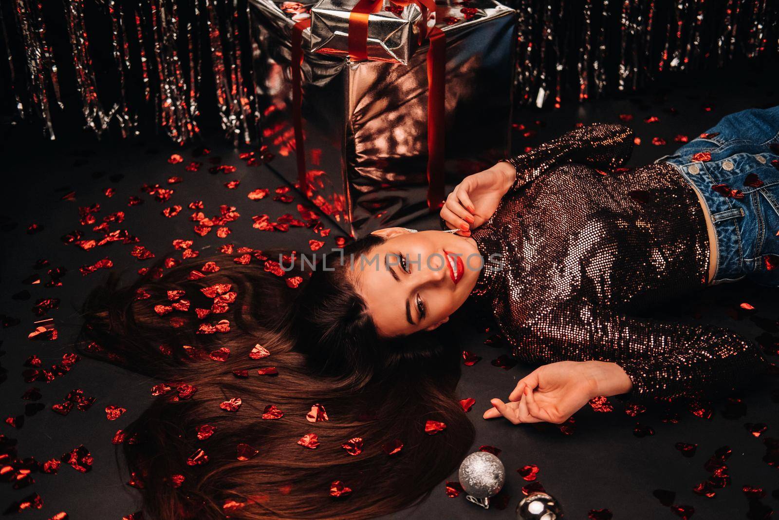 Top view of a girl lying in shiny clothes on the floor in confetti in the form of hearts.