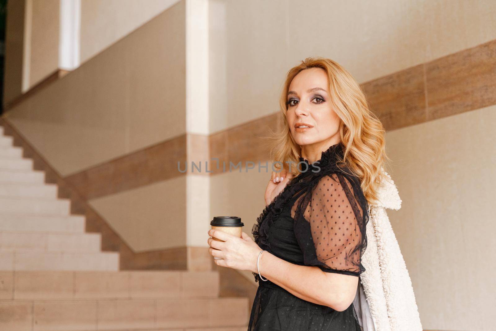 Portrait of a beautiful smiling blonde. She's walking up the stairs, coffee in hand. The Concept Of Urban Life. by Matiunina