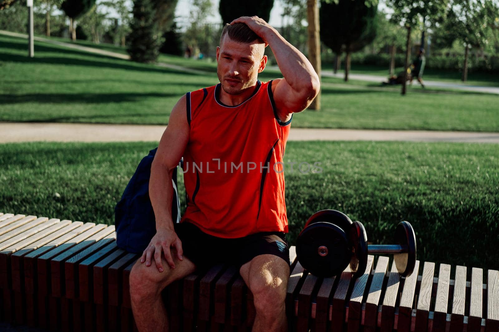 Cheerful male athlete in the park sits on a bench. High quality photo