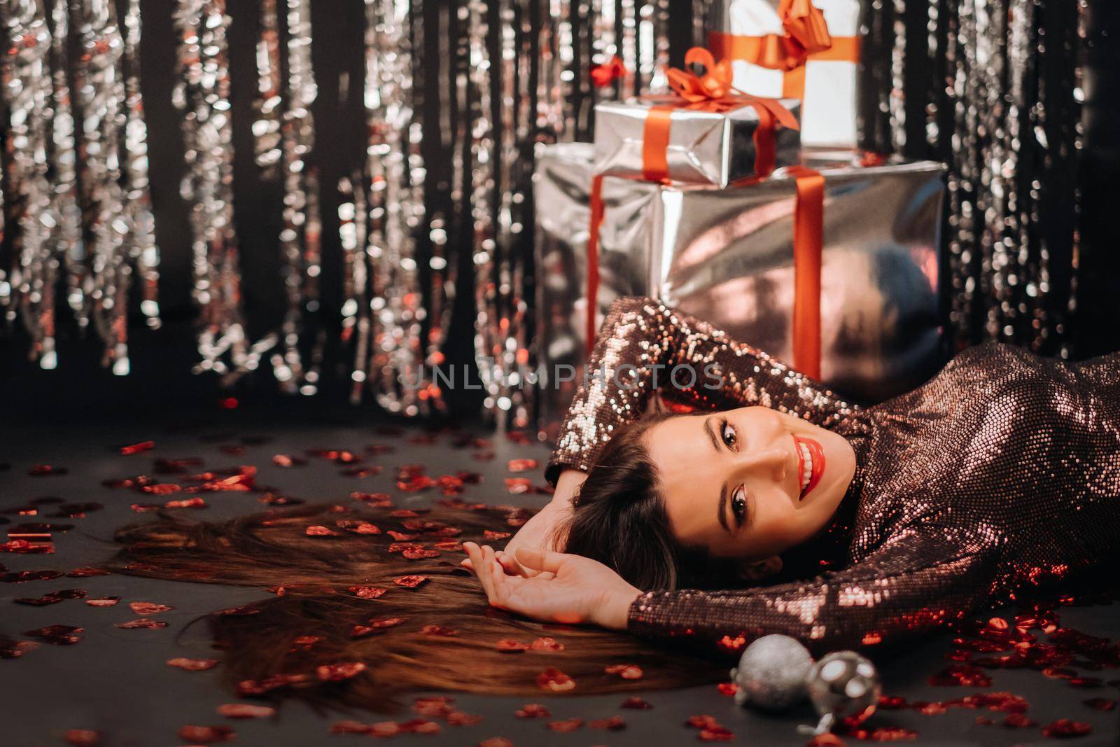 Top view of a girl lying in shiny clothes on the floor in confetti in the form of hearts and gifts by Lobachad