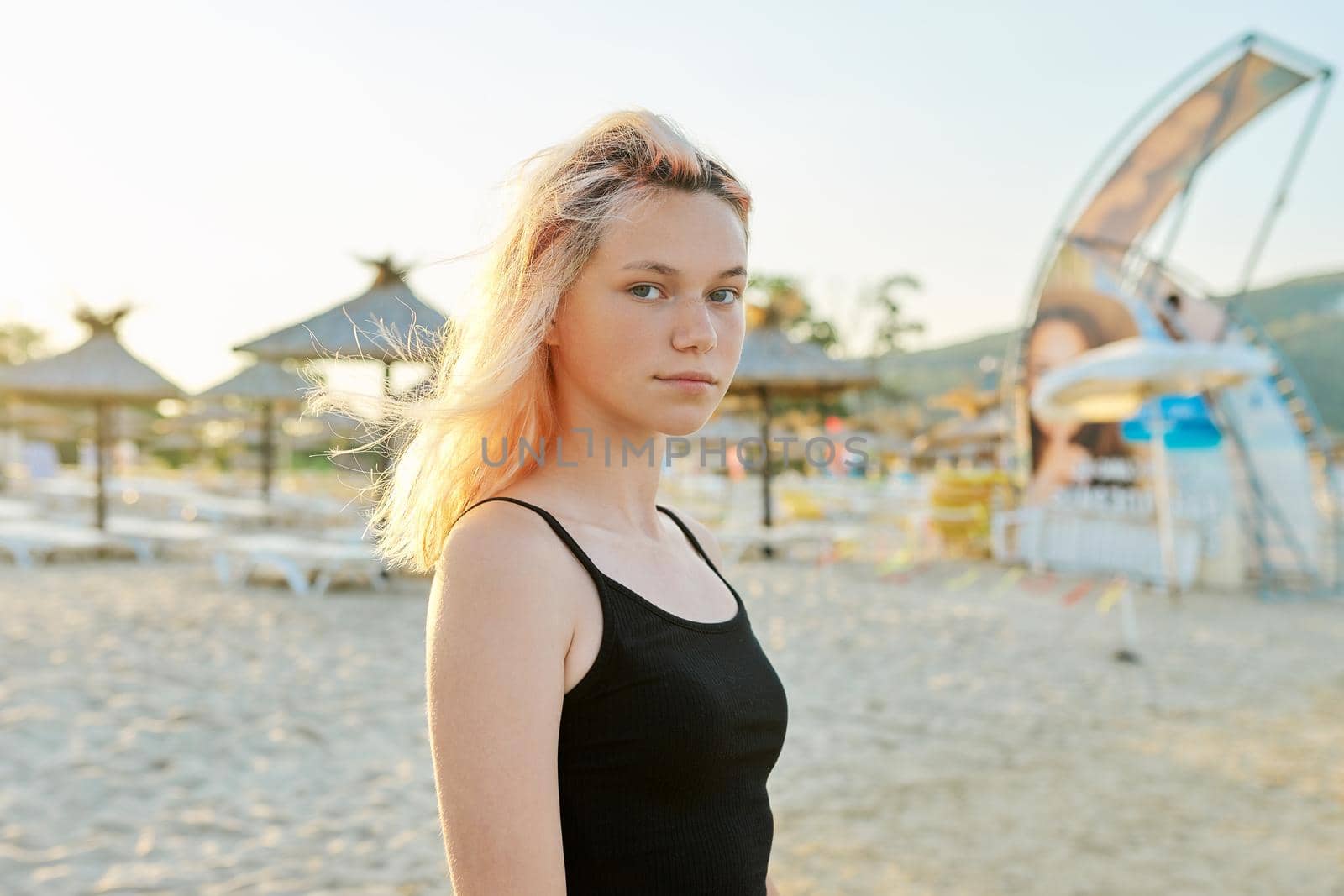 Portrait of young smiling blonde teenager in black top on the beach by VH-studio