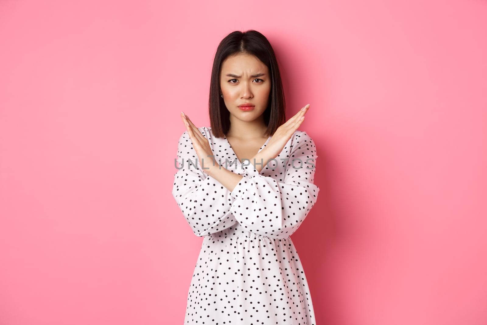 Angry asian woman tell stop, making cross to prohibit or disapprove something, frowning displeased, standing over pink background by Benzoix