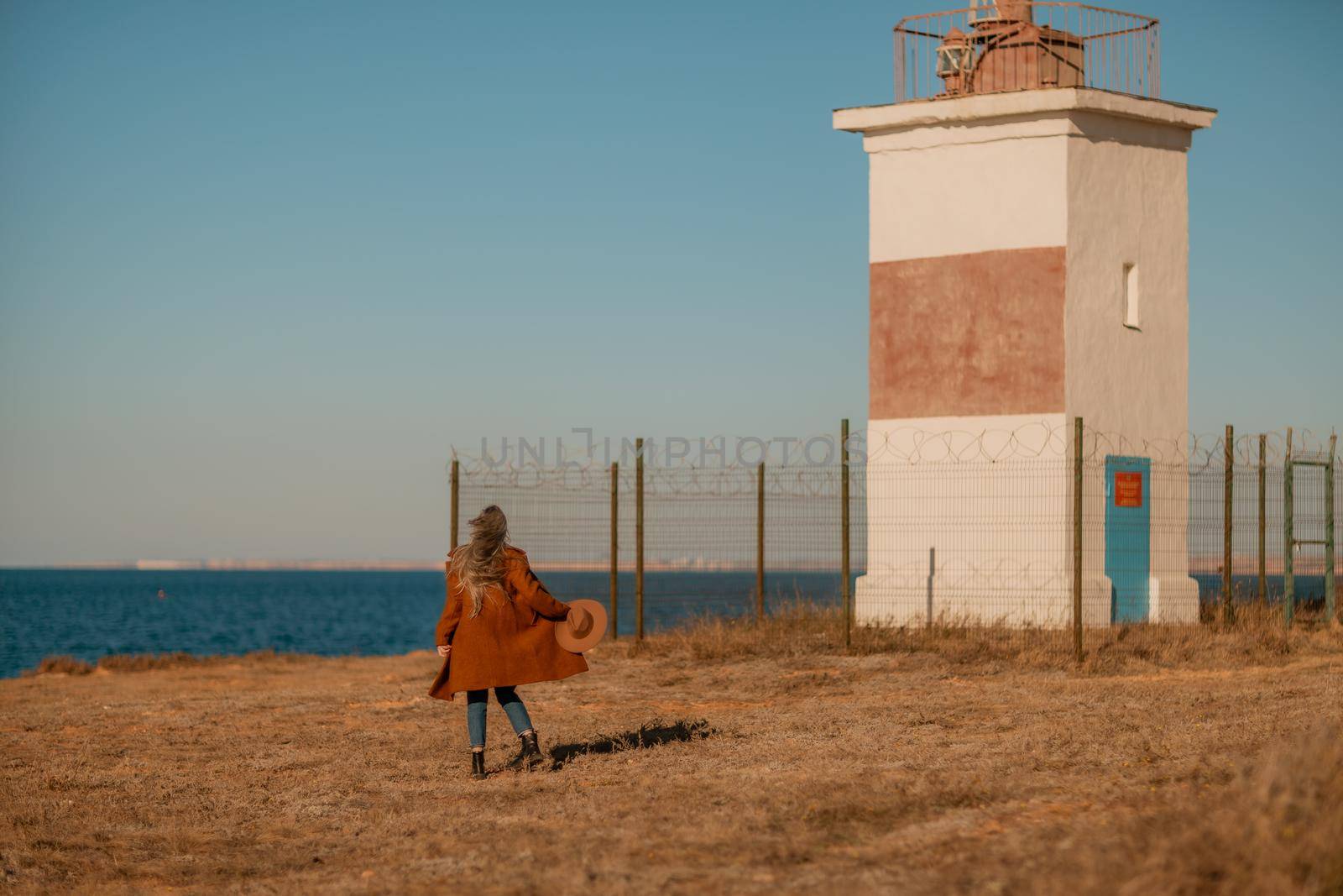 A woman walking along the coast near the sea. An elegant lady in a brown coat and a hat with fashionable makeup walks on the seashore.