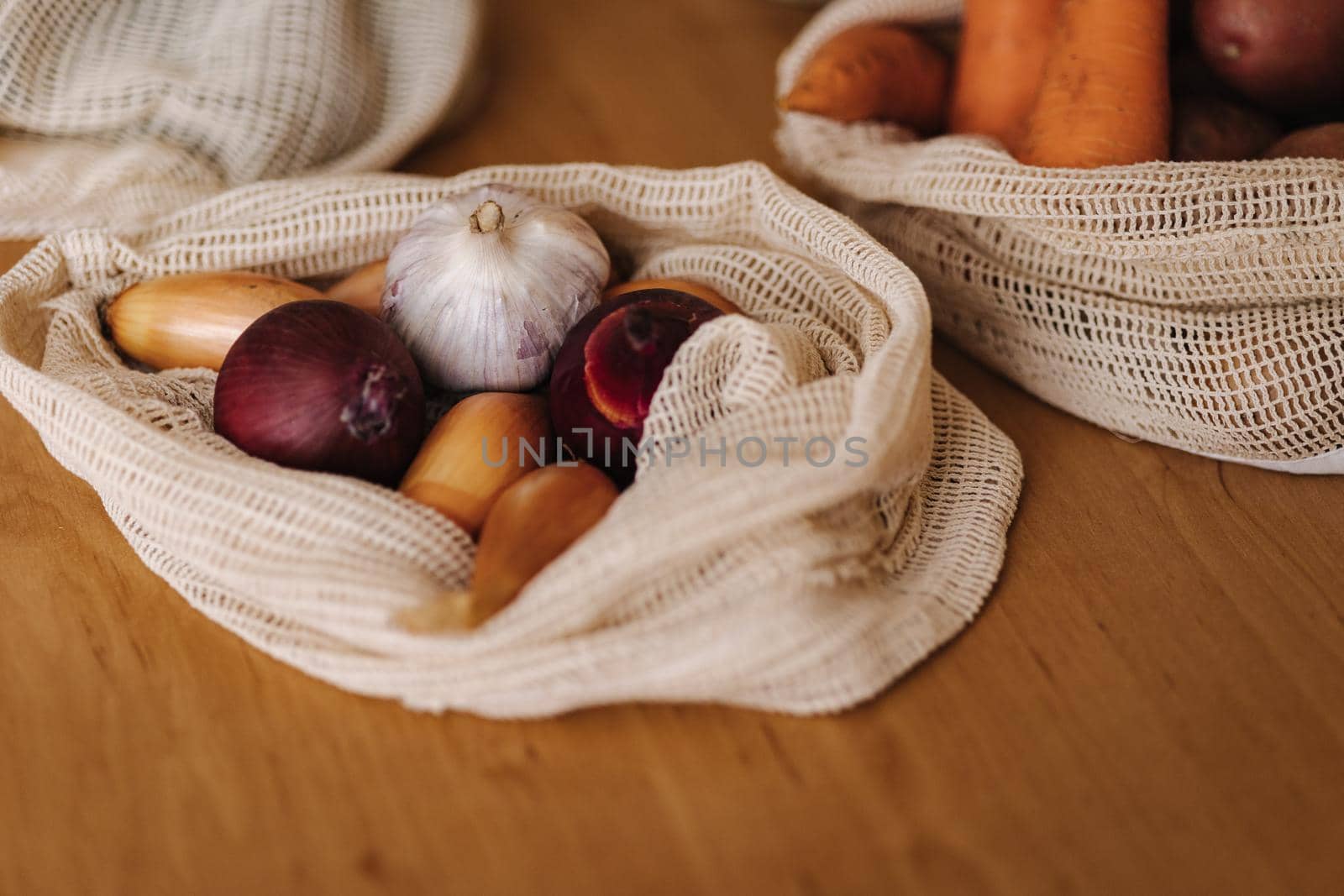 Garlic and onionin reusable grocery bag on a table at home. Mesh cotton with vegetables.