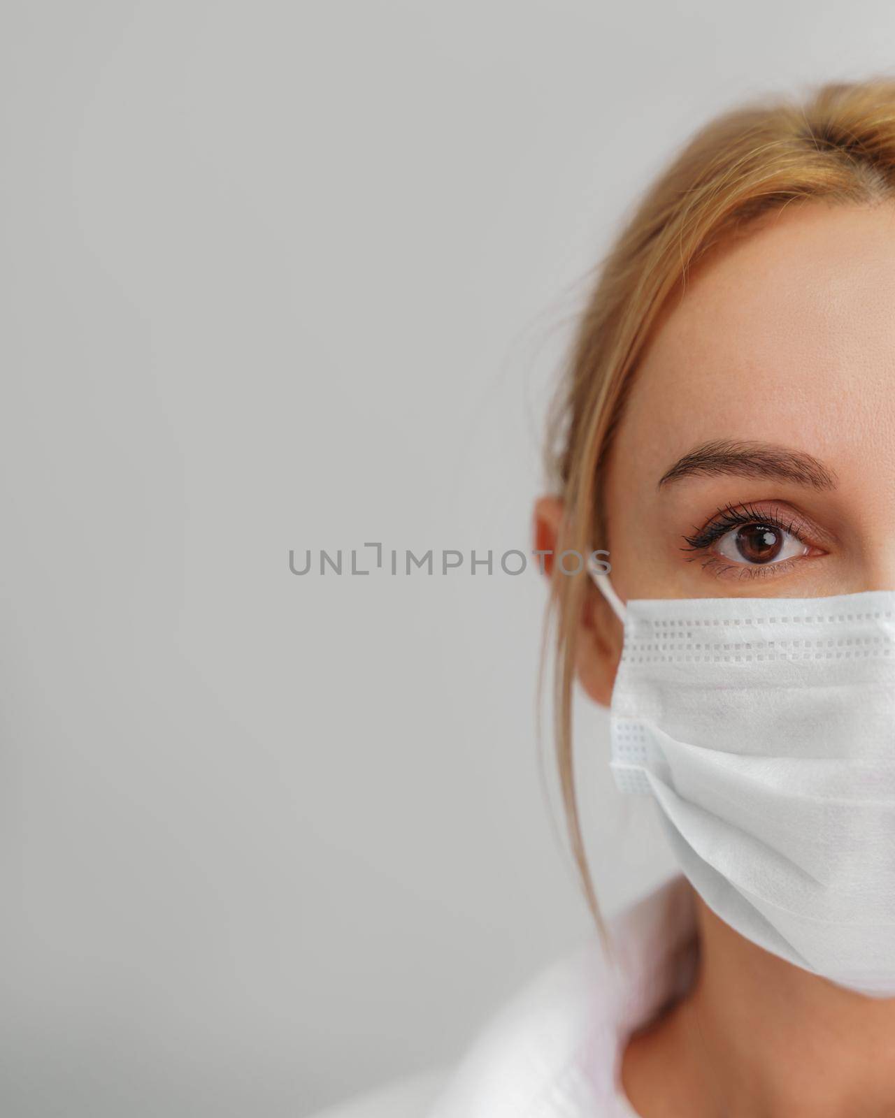 Close-up portrait of a young blonde woman in a medical mask on a light background. Virus protection. Coronovirus covid-19 The concept of a pandemic epidemic. Quarantine. Stay at home. by Matiunina