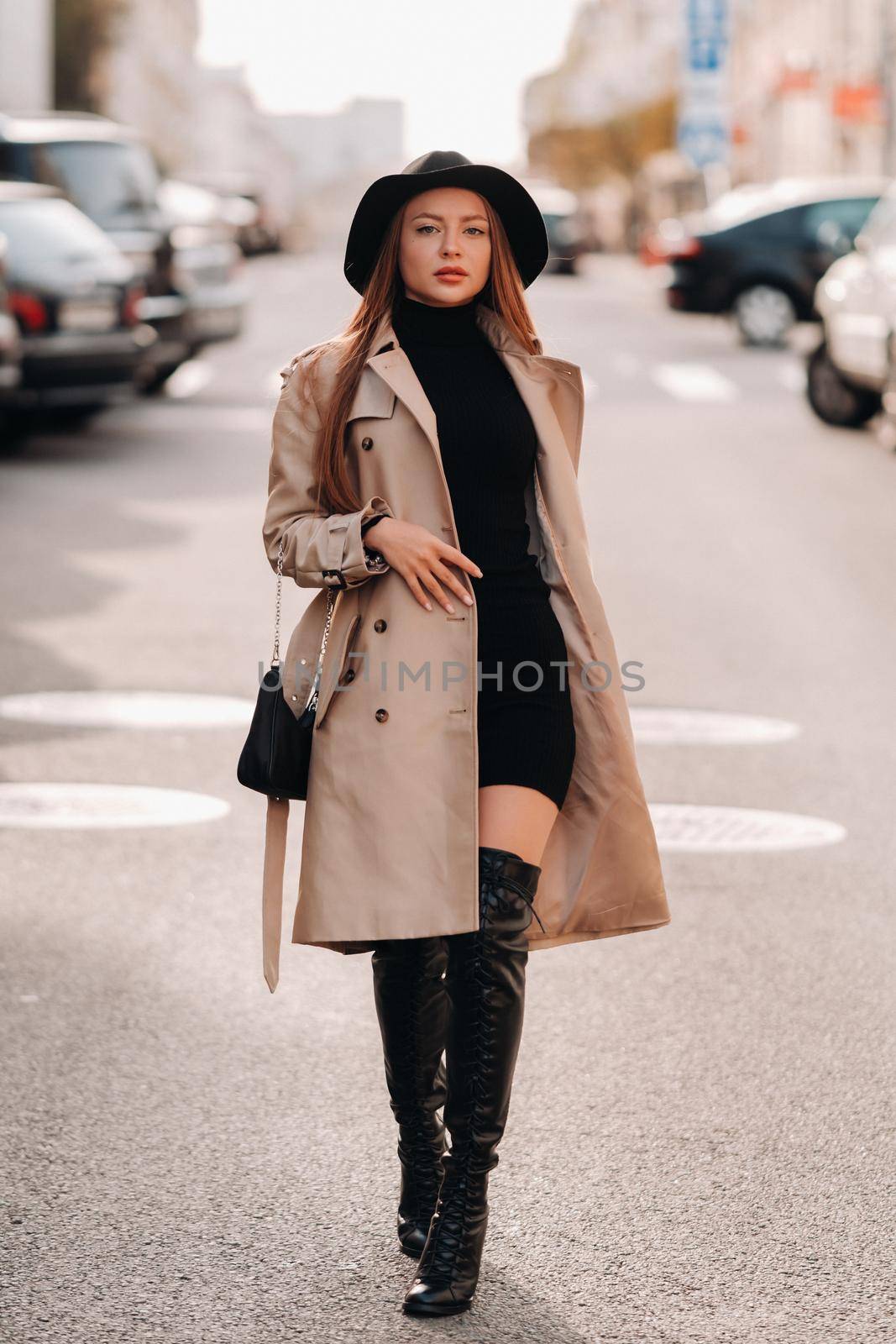 Stylish young woman in a beige coat in a black hat on a city street. Women's street fashion. Autumn clothing.Urban style.