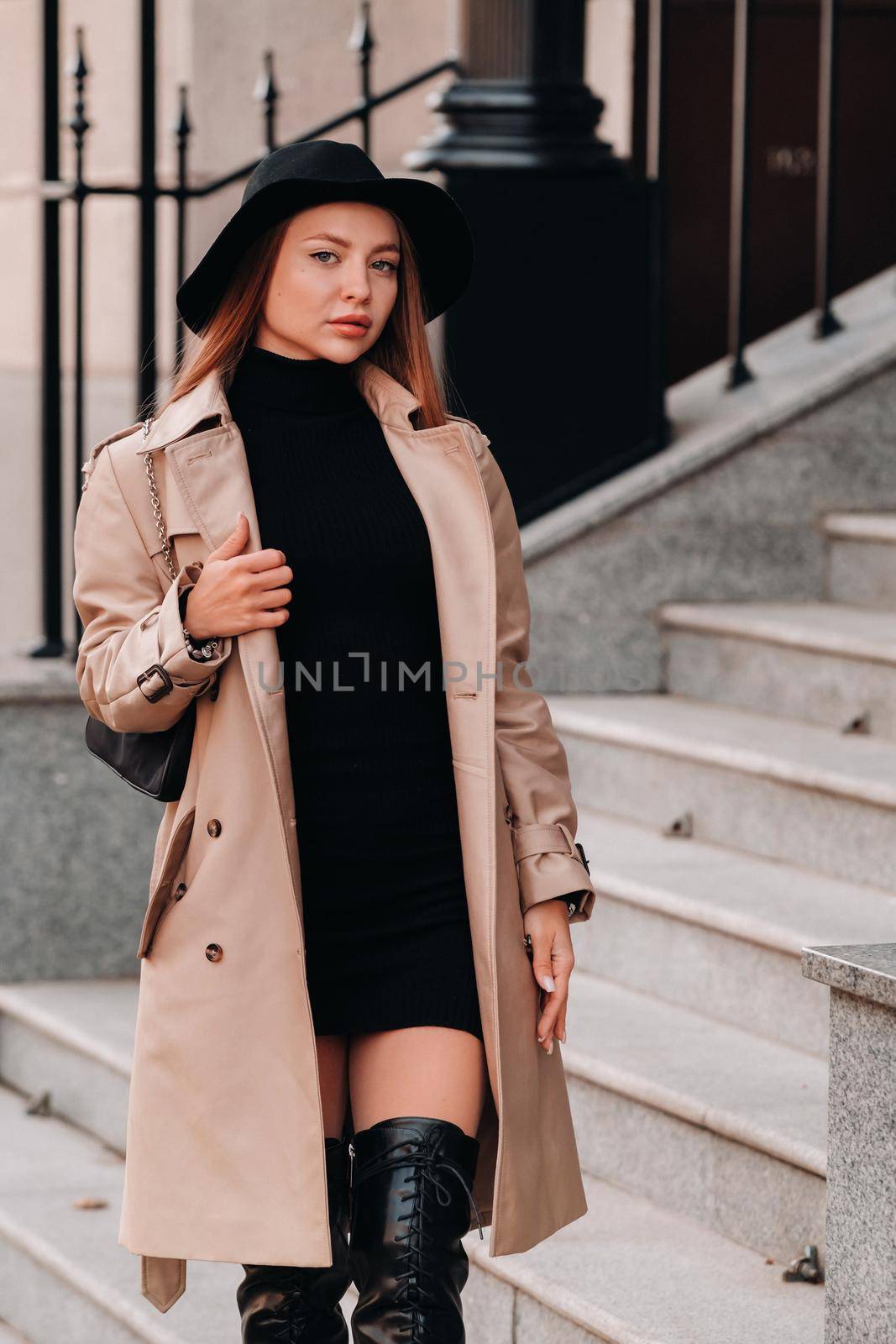 Stylish young woman in a beige coat in a black hat on a city street. Women's street fashion. Autumn clothing.Urban style.