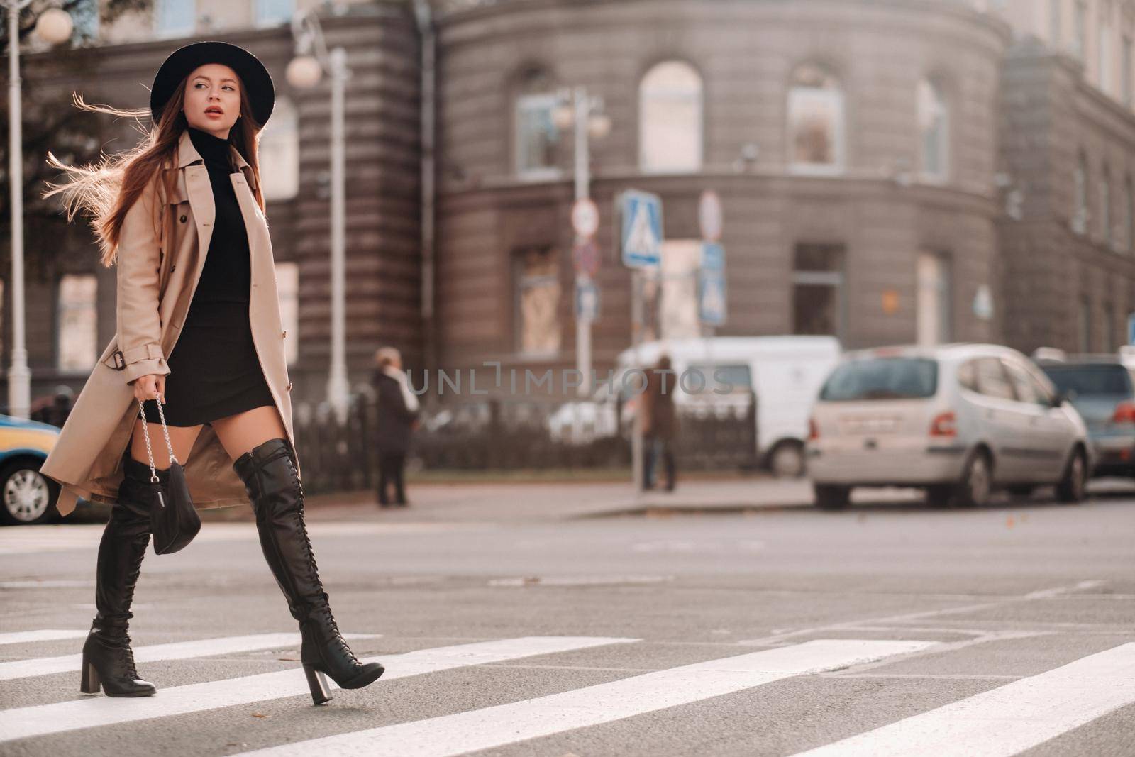 Stylish young woman in a beige coat in a black hat on a city street. Women's street fashion. Autumn clothing.Urban style.