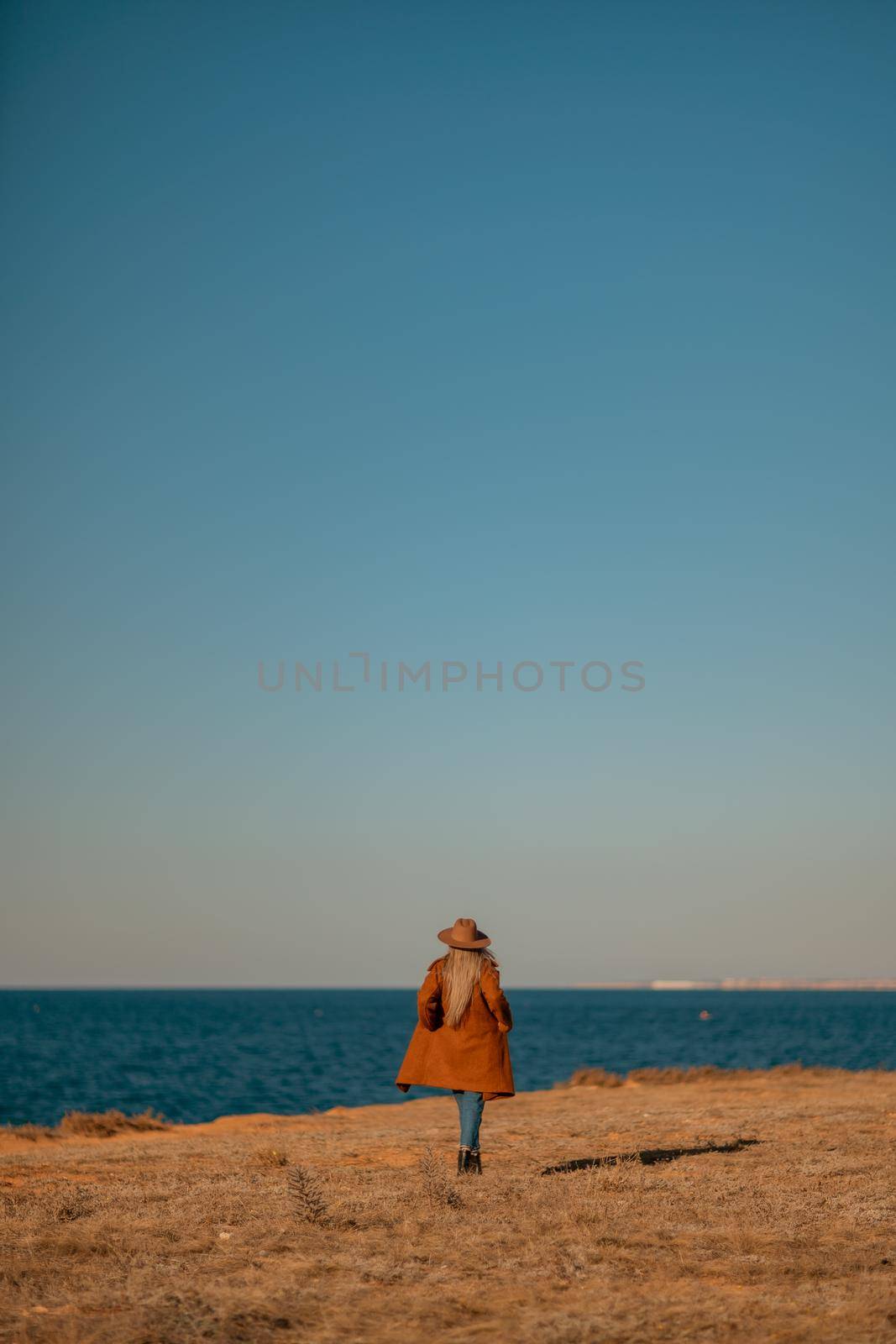 A woman walking along the coast near the sea. An elegant lady in a brown coat with fashionable makeup walks on the seashore.