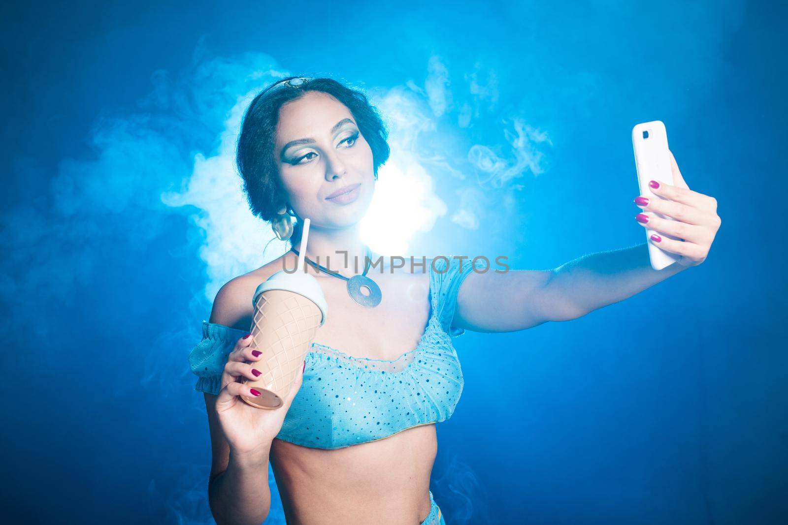 Magic, cosplay, carnival and fairy tale concept - Portrait of a young woman in the image of an Eastern fairy Princess takes selfie on blue background. by Satura86