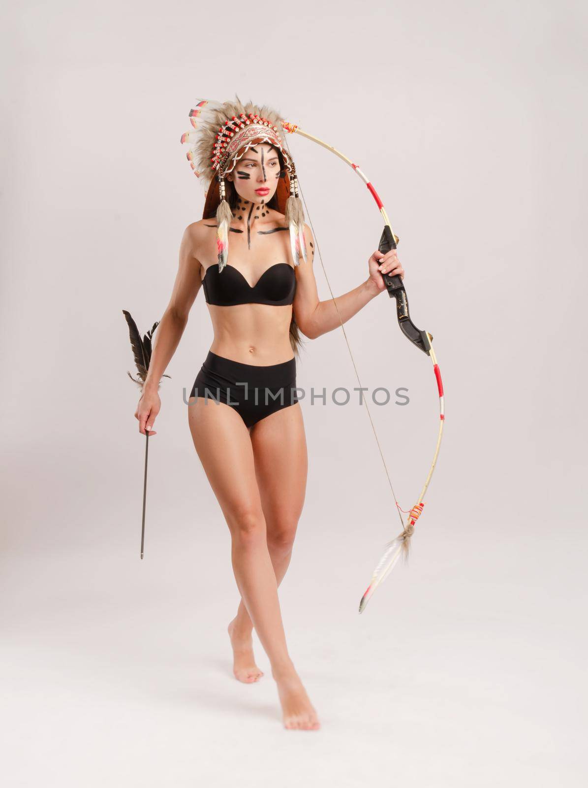 a woman in the image of indigenous peoples of America with a bow and arrow poses on a white background by Rotozey