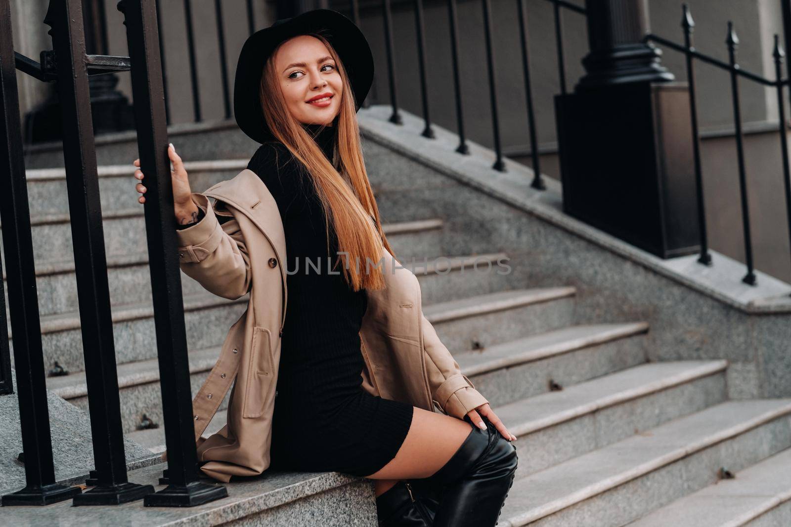 Stylish young woman in a beige coat in a black hat on a city street. Women's street fashion. Autumn clothing.Urban style.