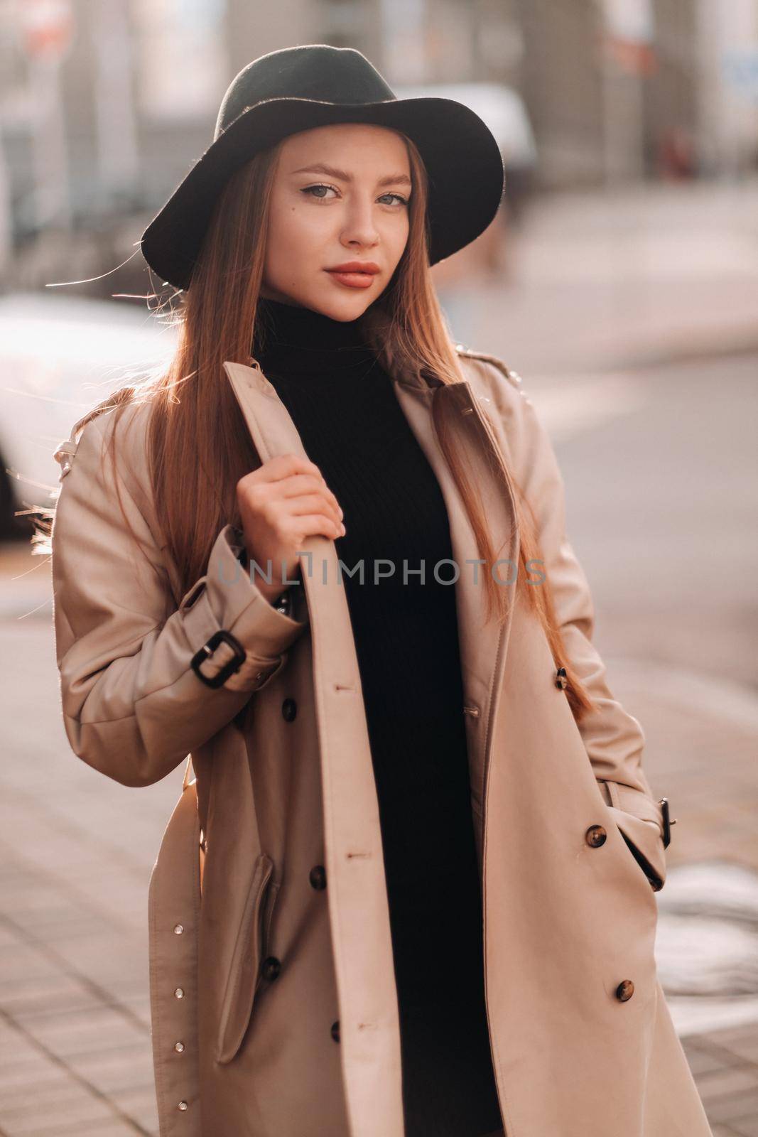 Stylish young woman in a beige coat in a black hat on a city street. Women's street fashion. Autumn clothing.Urban style.