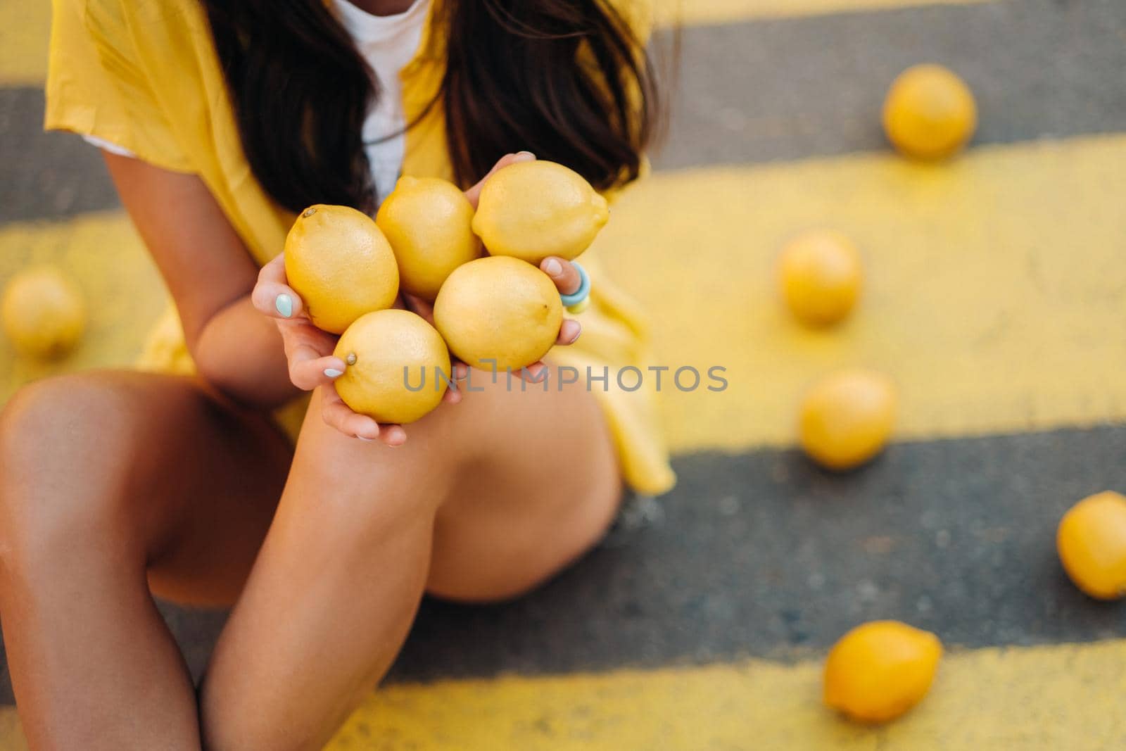a girl with lemons in a yellow shirt, shorts and black shoes sits on a yellow pedestrian crossing in the city. The lemon mood by Lobachad