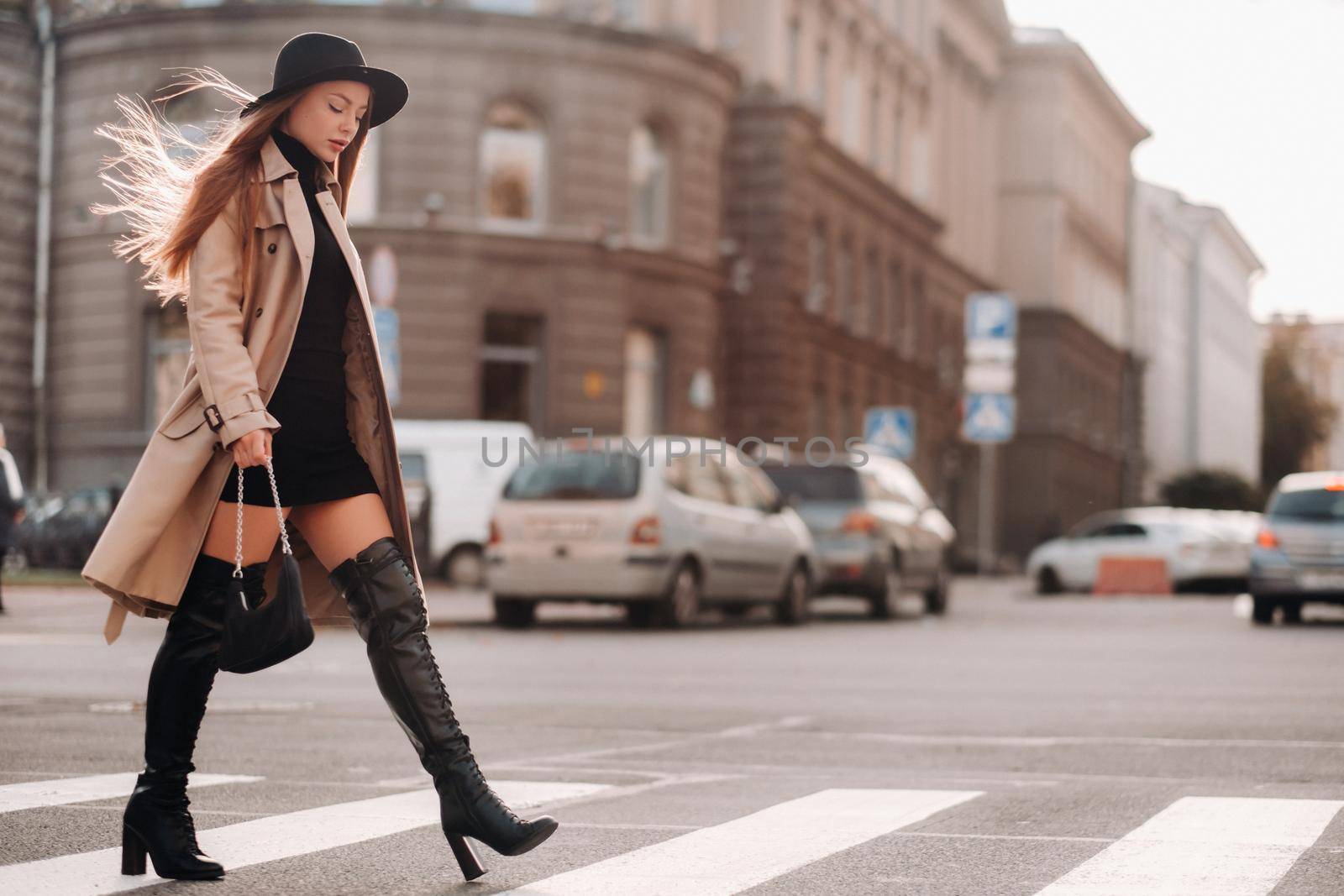 Stylish young woman in a beige coat in a black hat on a city street. Women's street fashion. Autumn clothing.Urban style.