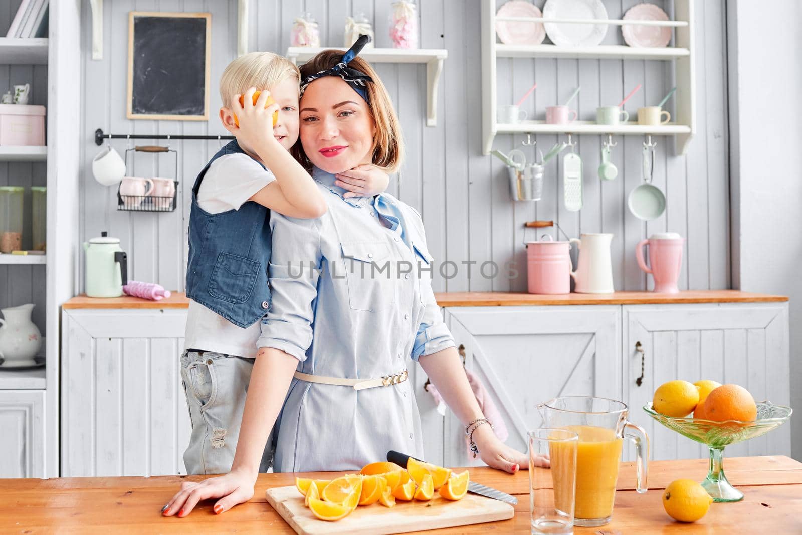 Healthy food, fresh fruit, juicy oranges. Mother and son are smiling while having a breakfast in kitchen. Bright morning in the kitchen