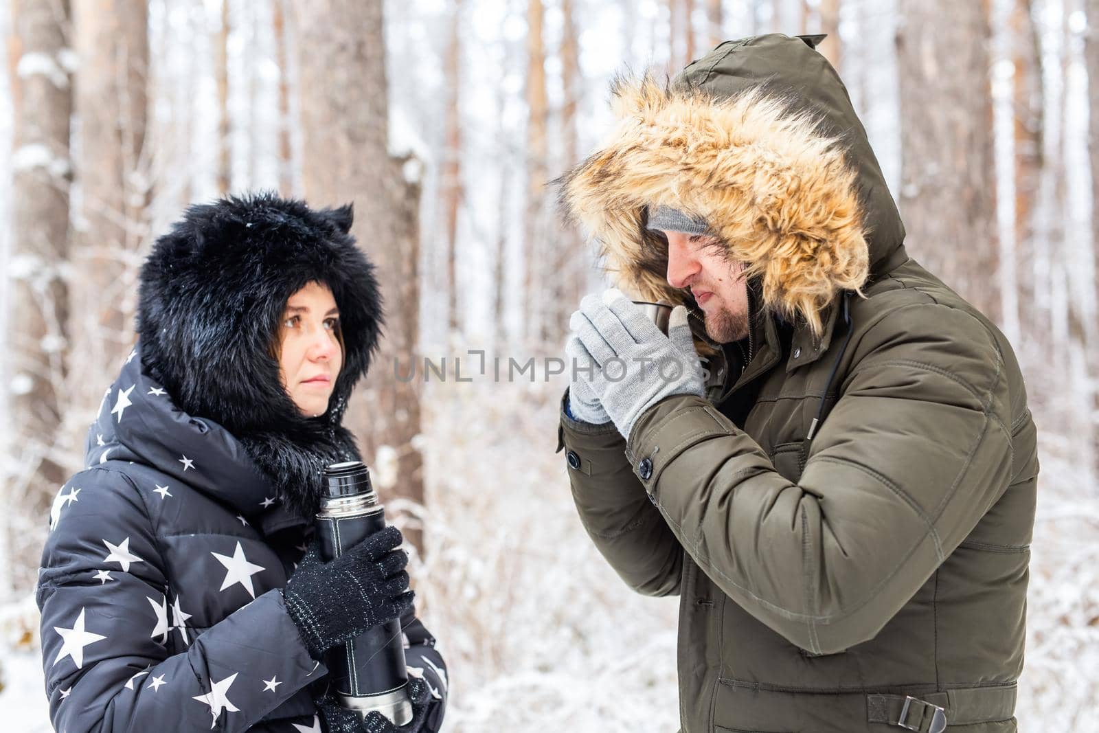 Season and walk concept - Happy couple drinking hot tea in winter forest.