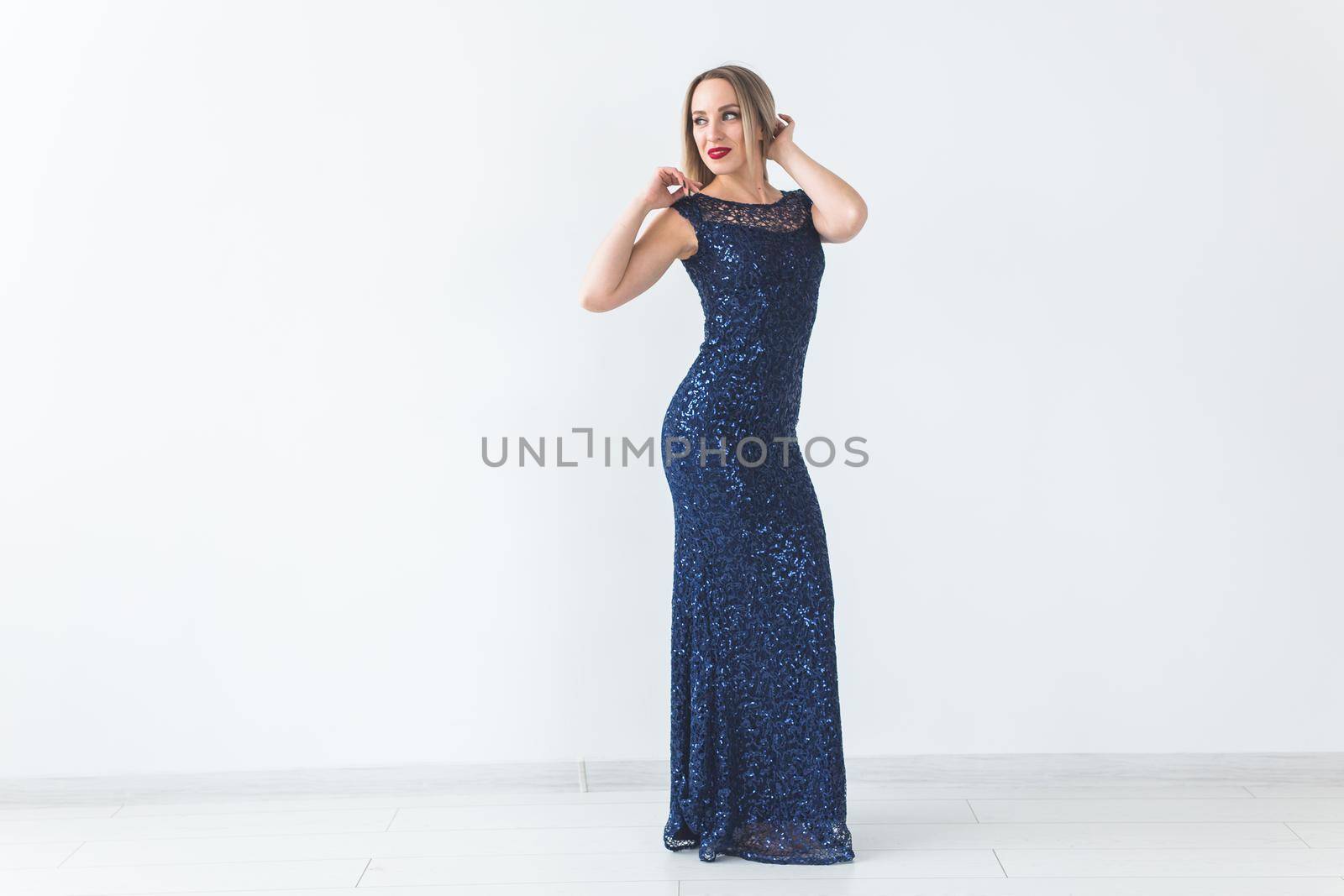 Fashionable young blonde woman in beautiful elegant dress posing at white