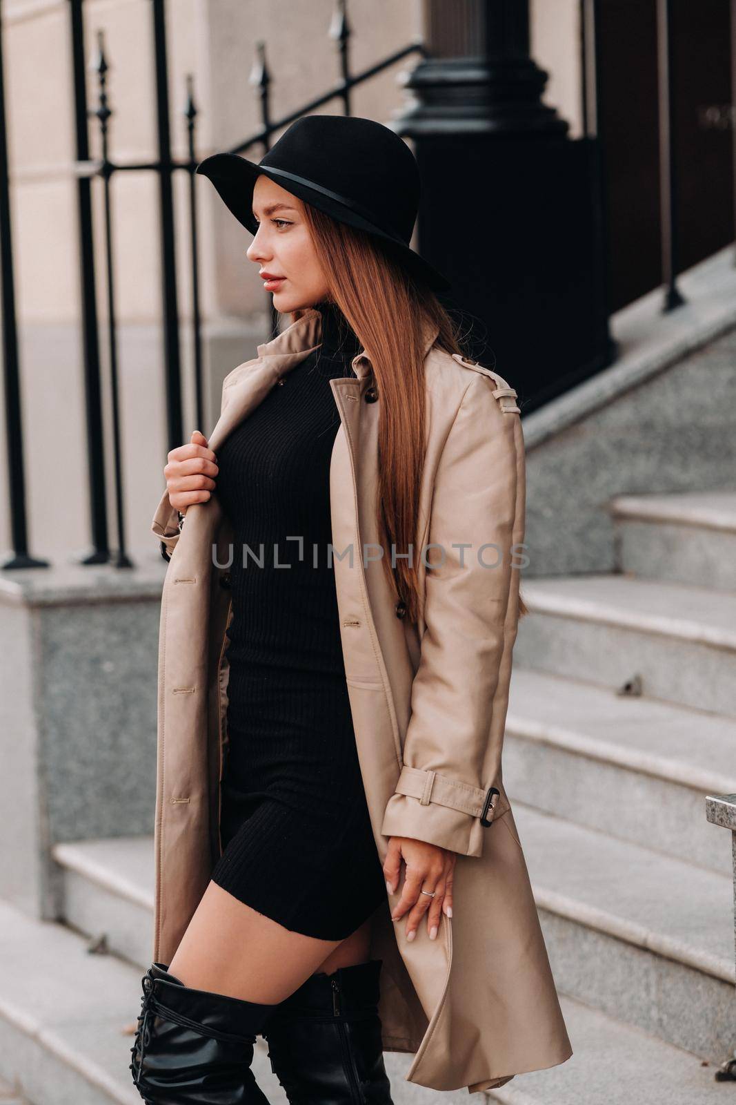 Stylish young woman in a beige coat in a black hat on a city street. Women's street fashion. Autumn clothing.Urban style.