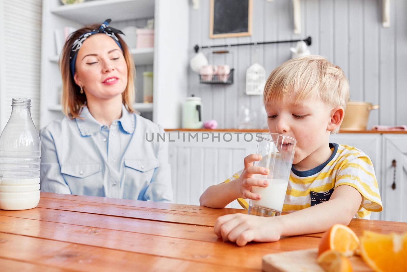 Little boy are smiling while having a breakfast in kitchen. Mom is pouring milk into glass.