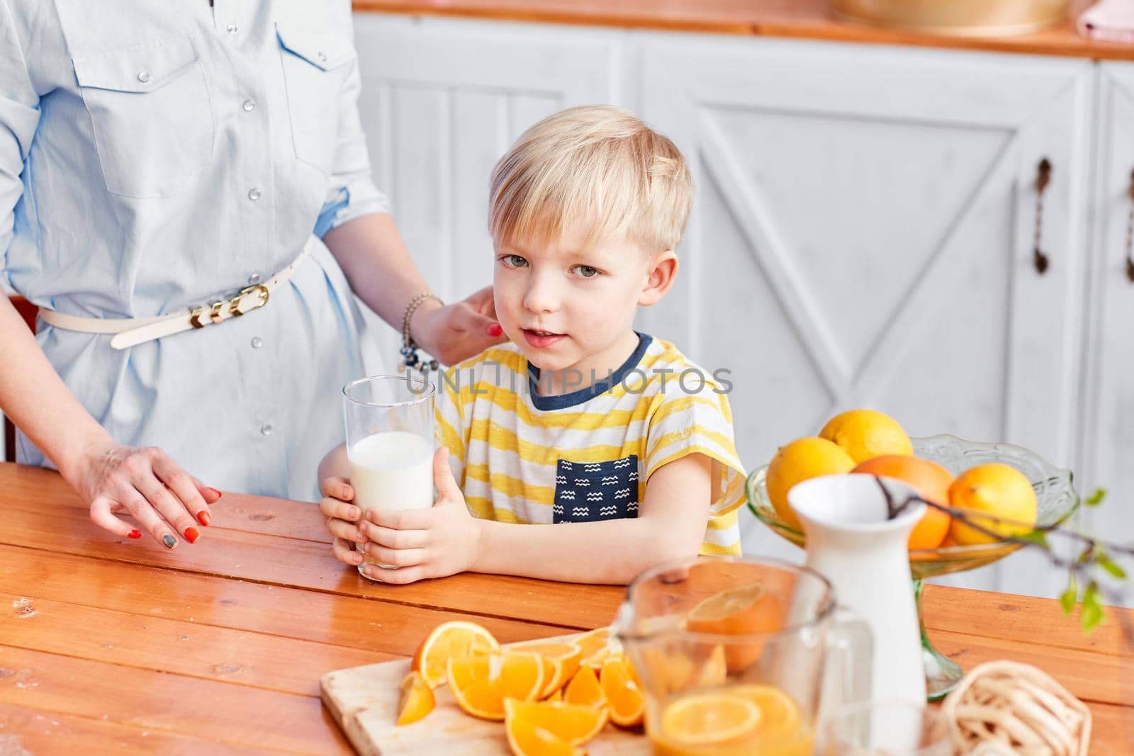 Healthy food, fresh fruit, juicy oranges. Boy are smiling while having a breakfast in kitchen. Bright morning in the kitchen. by Malkovkosta