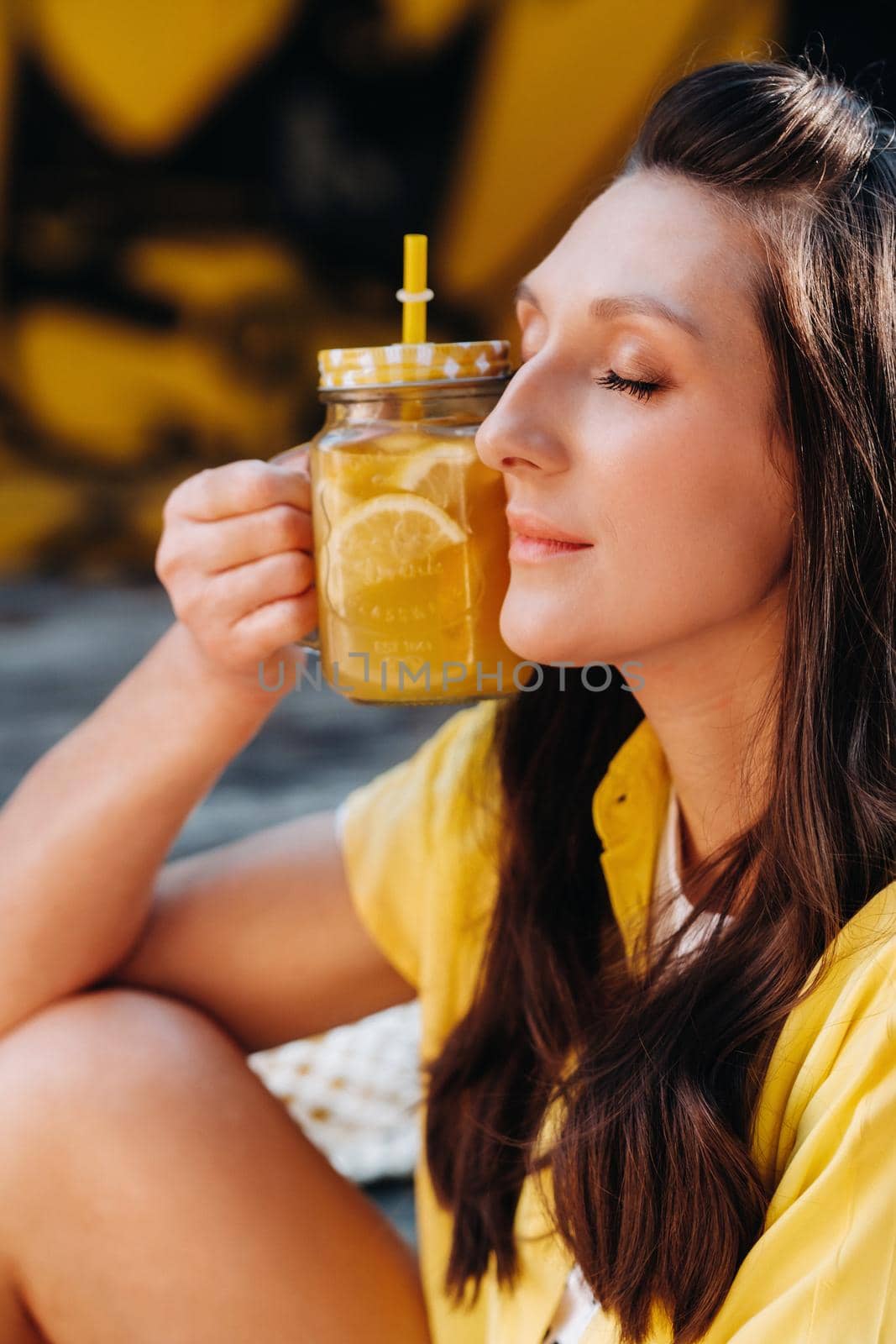 a girl in a yellow shirt with lemon juice in her hands in a city cafe on the street. Portrait of a woman in yellow by Lobachad